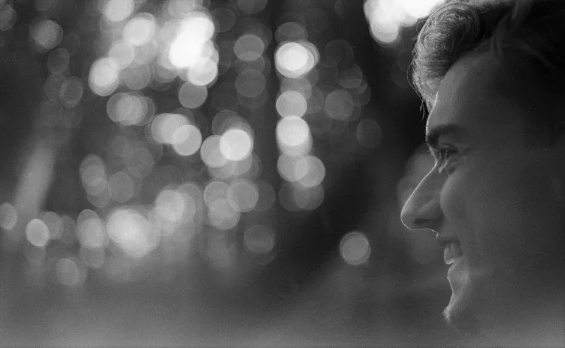Profile of a smiling young man outdoors with a bokeh background of circular light reflections.