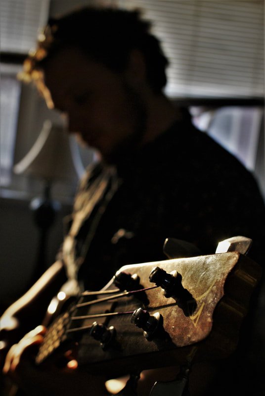 Silhouette of a person playing an acoustic guitar indoors with sunlight coming through window blinds.