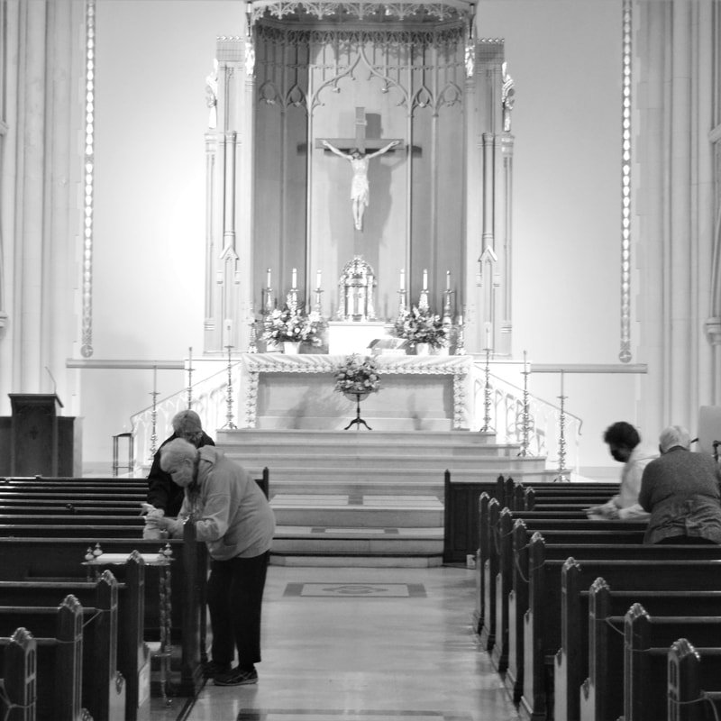 Interior of a church with people praying at pews, altar with flowers, candles, and a crucifix