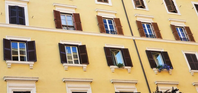 Multiple windows with open and closed shutters on a yellow European building.
