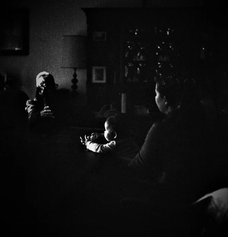 A black and white photo of a woman sitting with a child, possibly in a living room, with a person on the TV screen in the background, watching TV together.
