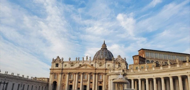 The front of St. Peter's Basilica in Vatican City with a blue sky and clouds in the background.