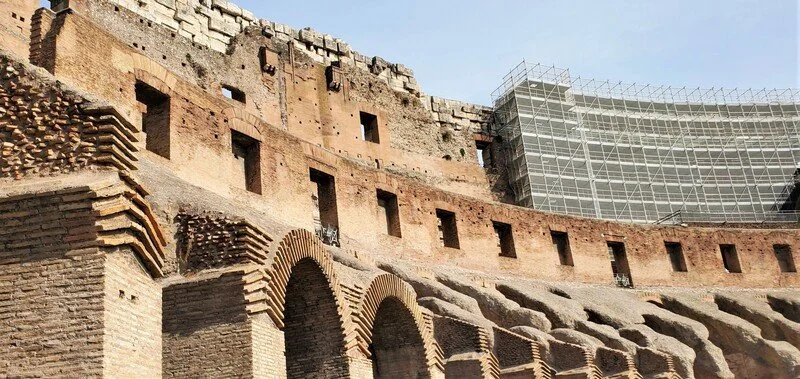 The image shows a view of the ancient Roman amphitheater, the Colosseum, with part of it under renovation, evident by scaffolding on one side.