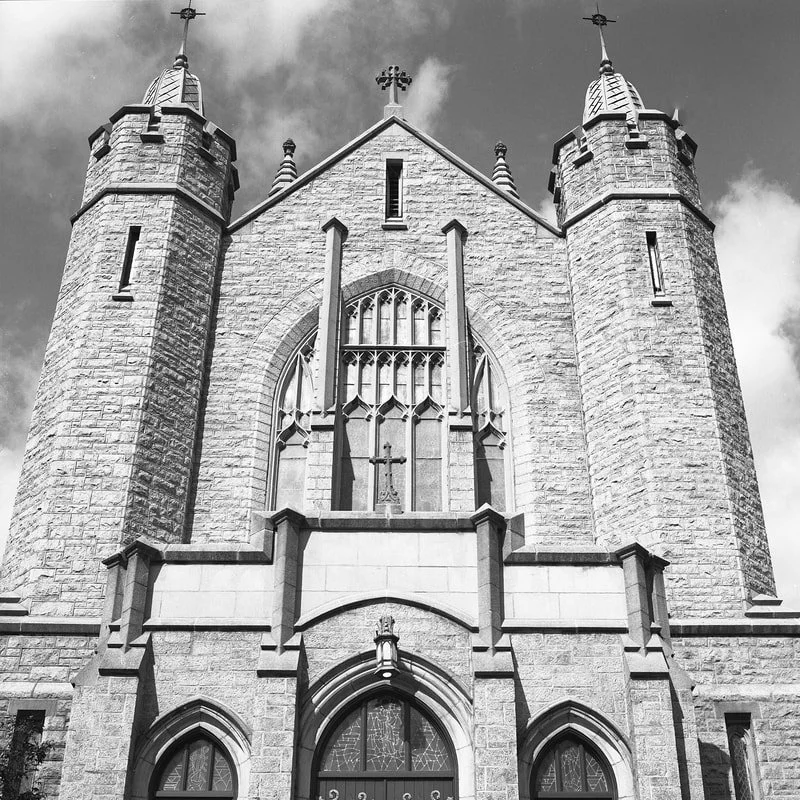 Front view of a historic stone church with two tall towers, arched windows, and a cross at the top.