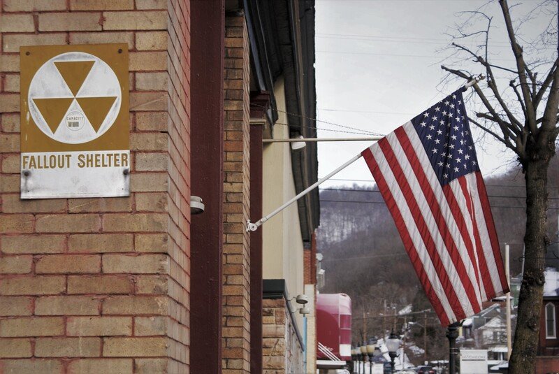American flag hanging outside a building with a sign indicating a Fallout shelter