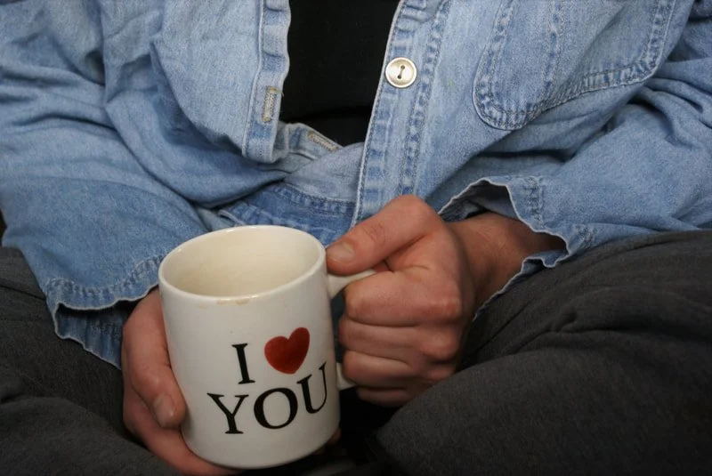 Person wearing a light denim jacket holding a white mug with 'I ♥ YOU' printed on it.