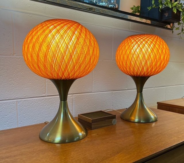 Two modern table lamps with orange, woven, dome-shaped lamp shades and metallic bases on a wooden surface.