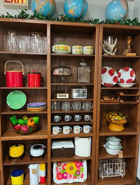 Wooden shelving unit filled with glassware, dishes, kitchenware, and decorative items.