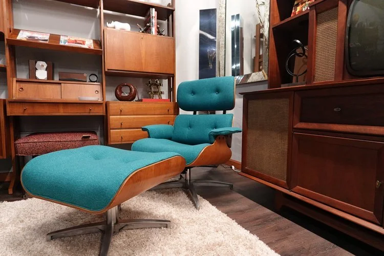 A vintage teal lounge chair with matching ottoman in a room with wooden shelves and cabinets.