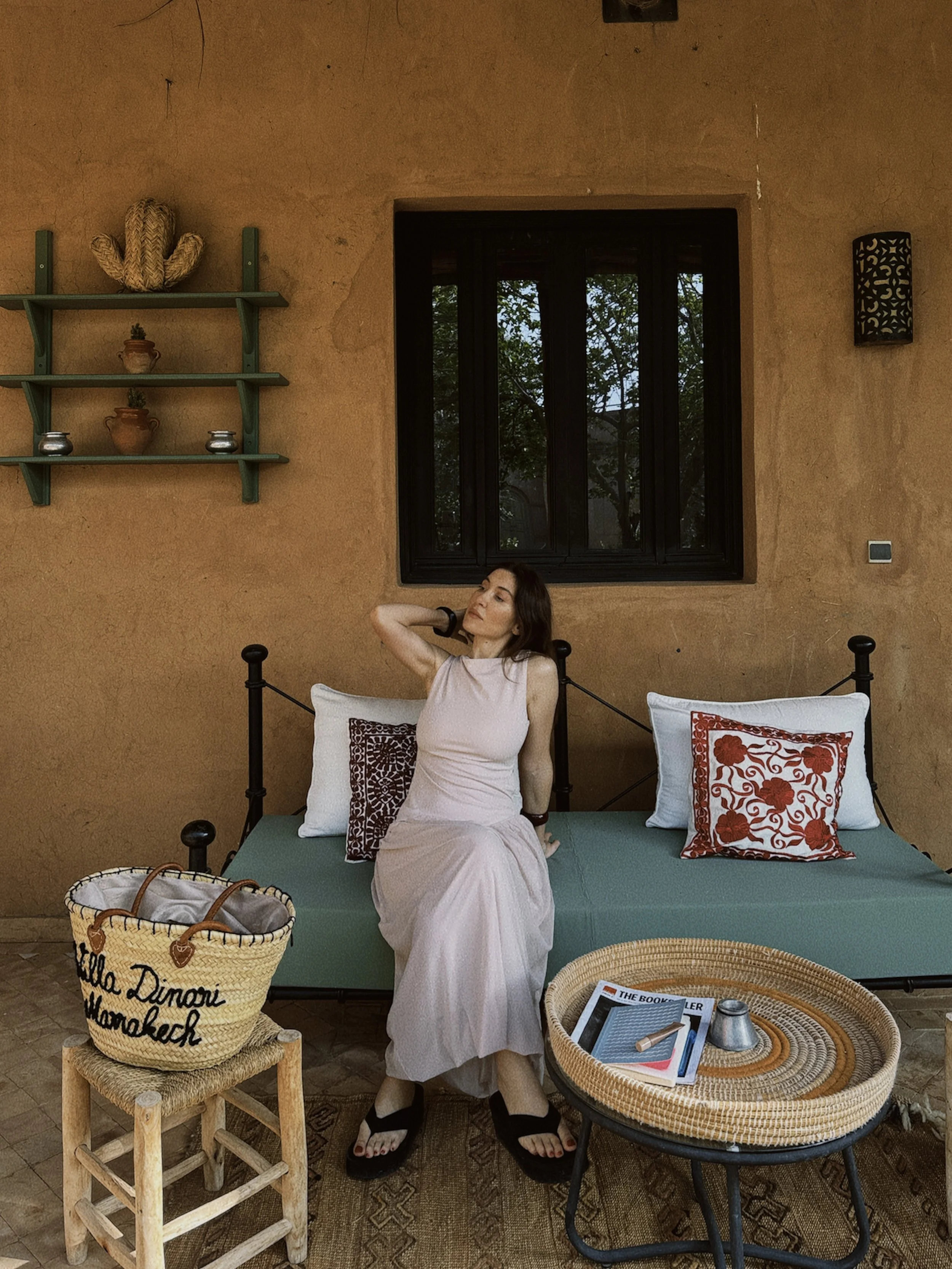Woman seated outdoors gently striking a singing bowl with a mallet, wearing a white dress, and surrounded by dim natural lighting.