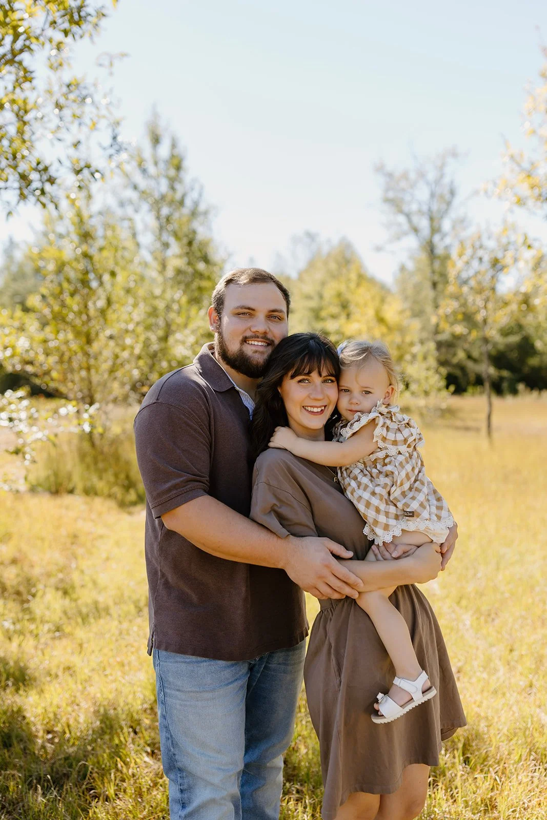 Family of three shares a big hug in a golden fall field, everyone smiling