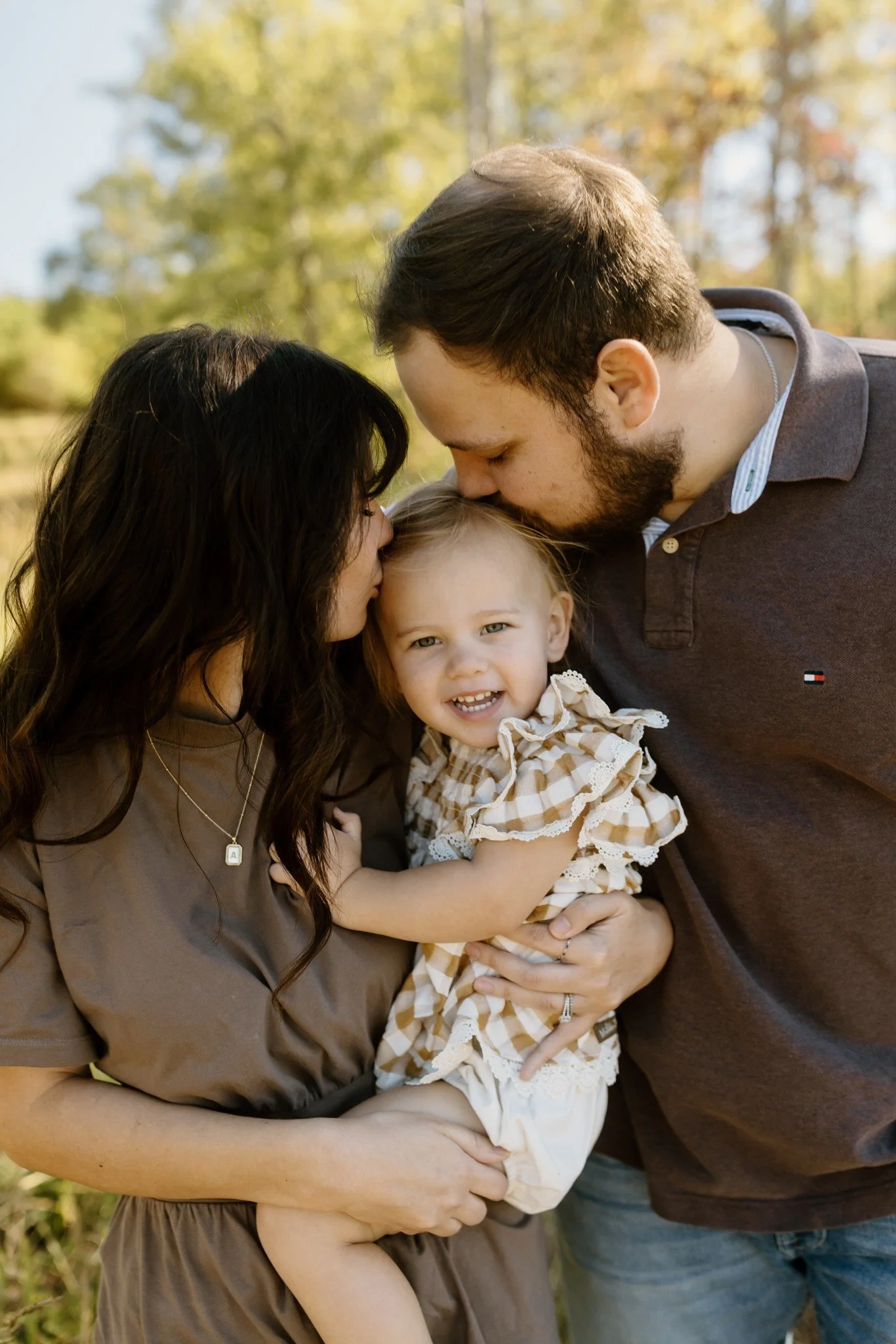 Dad kisses the top of his little girl's head while mom leans in close during fall family photos
