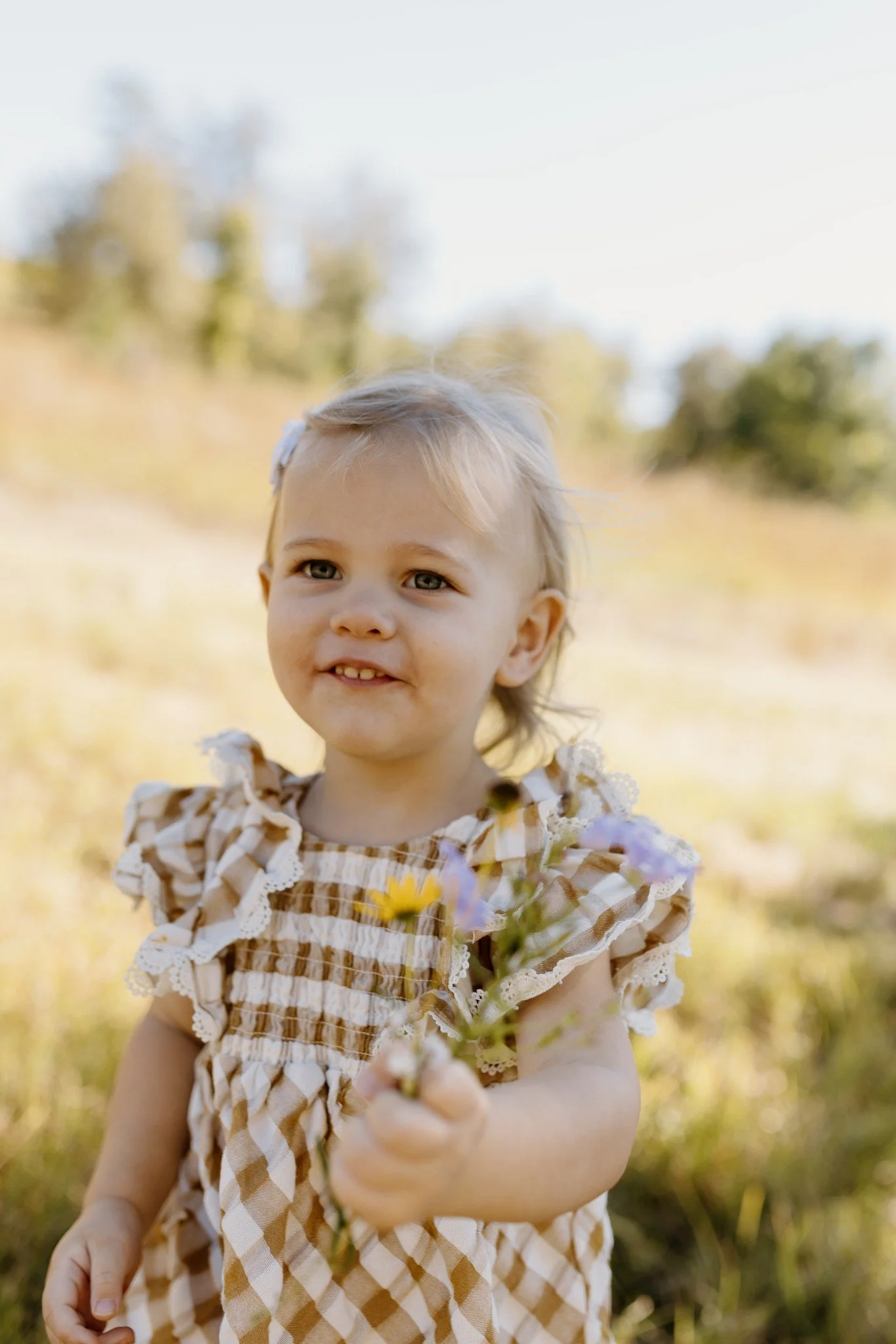 Smiling toddler holds a handful of wildflowers during her fall family session