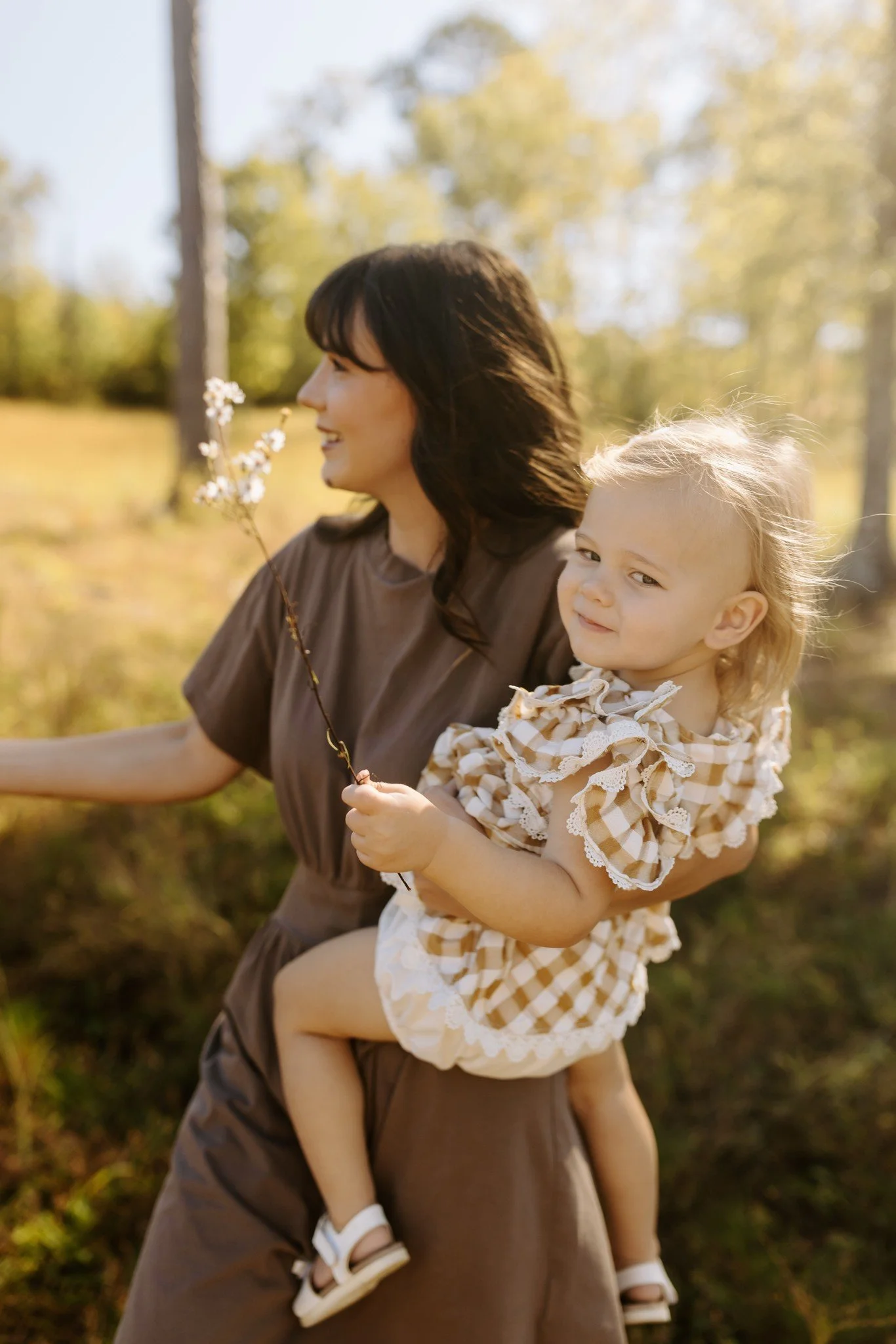 Little hands hold a tiny white wildflower against a gingham dress