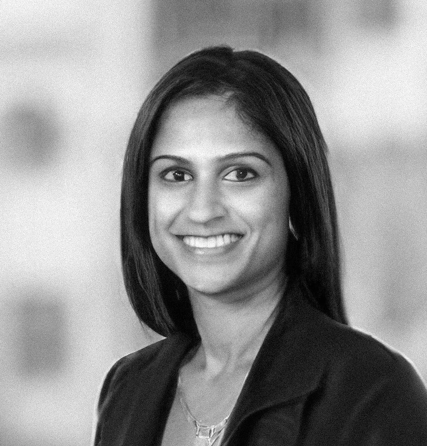 Black and white portrait of a smiling woman with shoulder-length straight hair, wearing a blazer and a necklace.