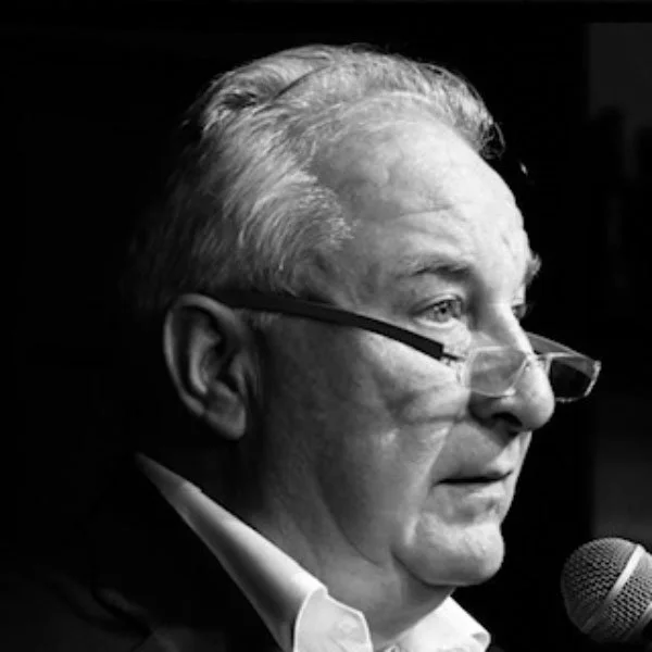 Side profile of an older man with glasses speaking into a microphone