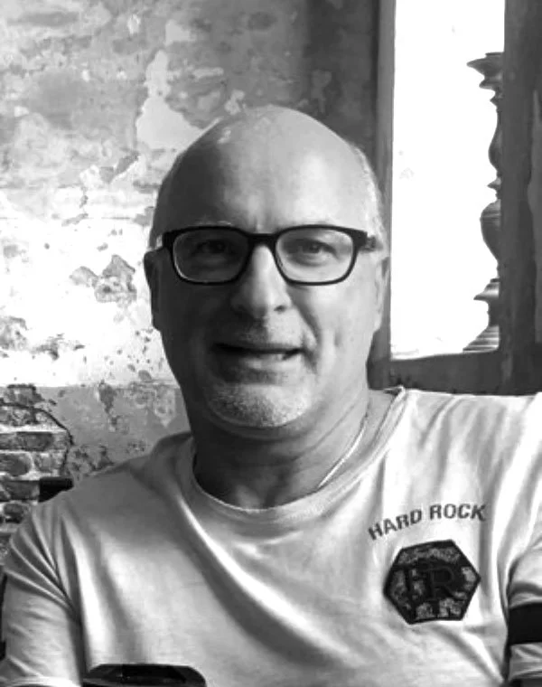 A man with glasses and a shaved head smiling at the camera, wearing a T-shirt that says 'Hard Rock'.