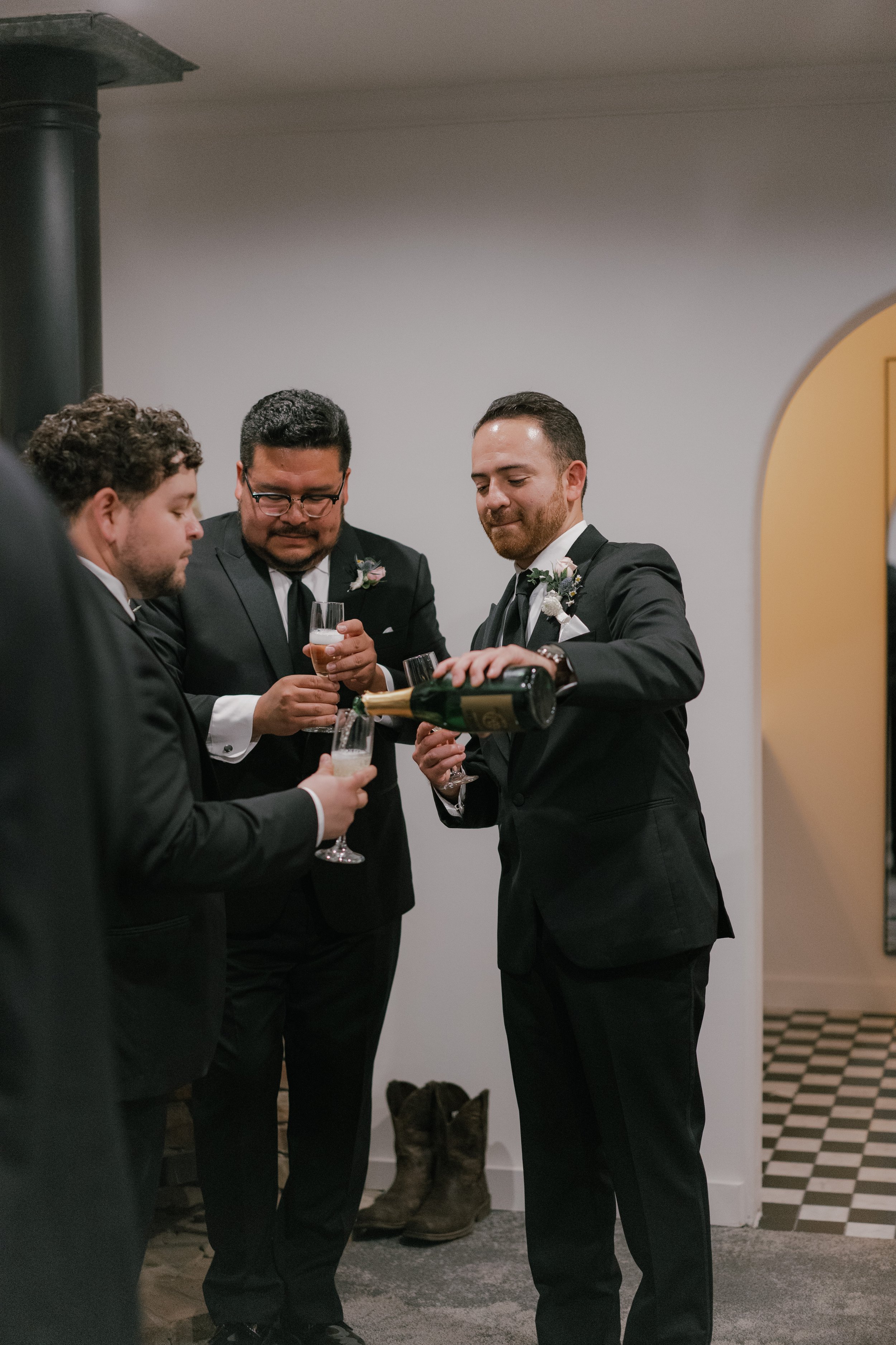 Group of men in tuxedos pouring and holding glasses of champagne at a celebration.