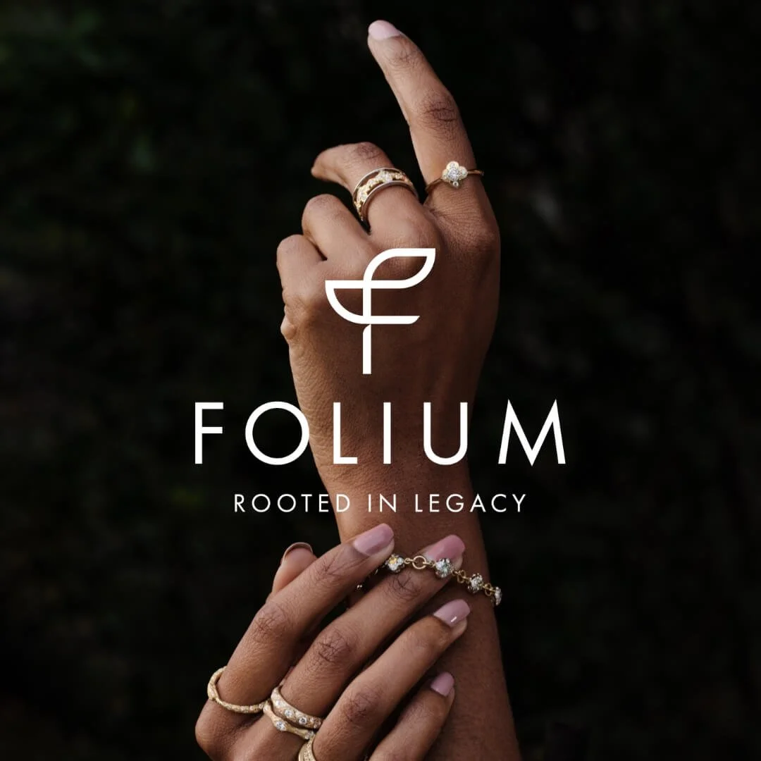 Close-up of hands wearing layered gold and diamond rings and bracelets against a dark background with Folium logo and “Rooted in Legacy” text overlay.