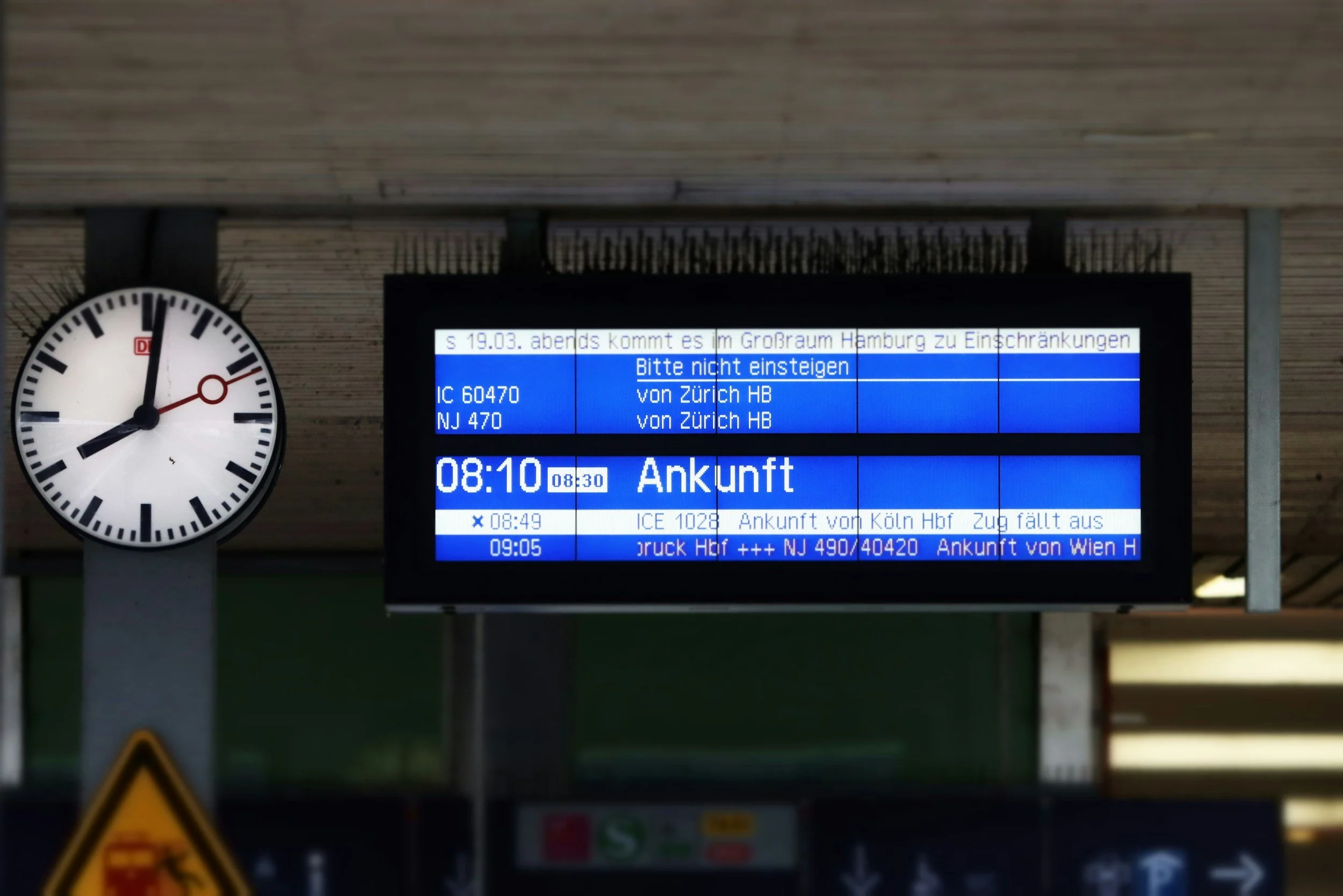 Anzeigetafel in einem Bahnhof neben einer großen Uhr