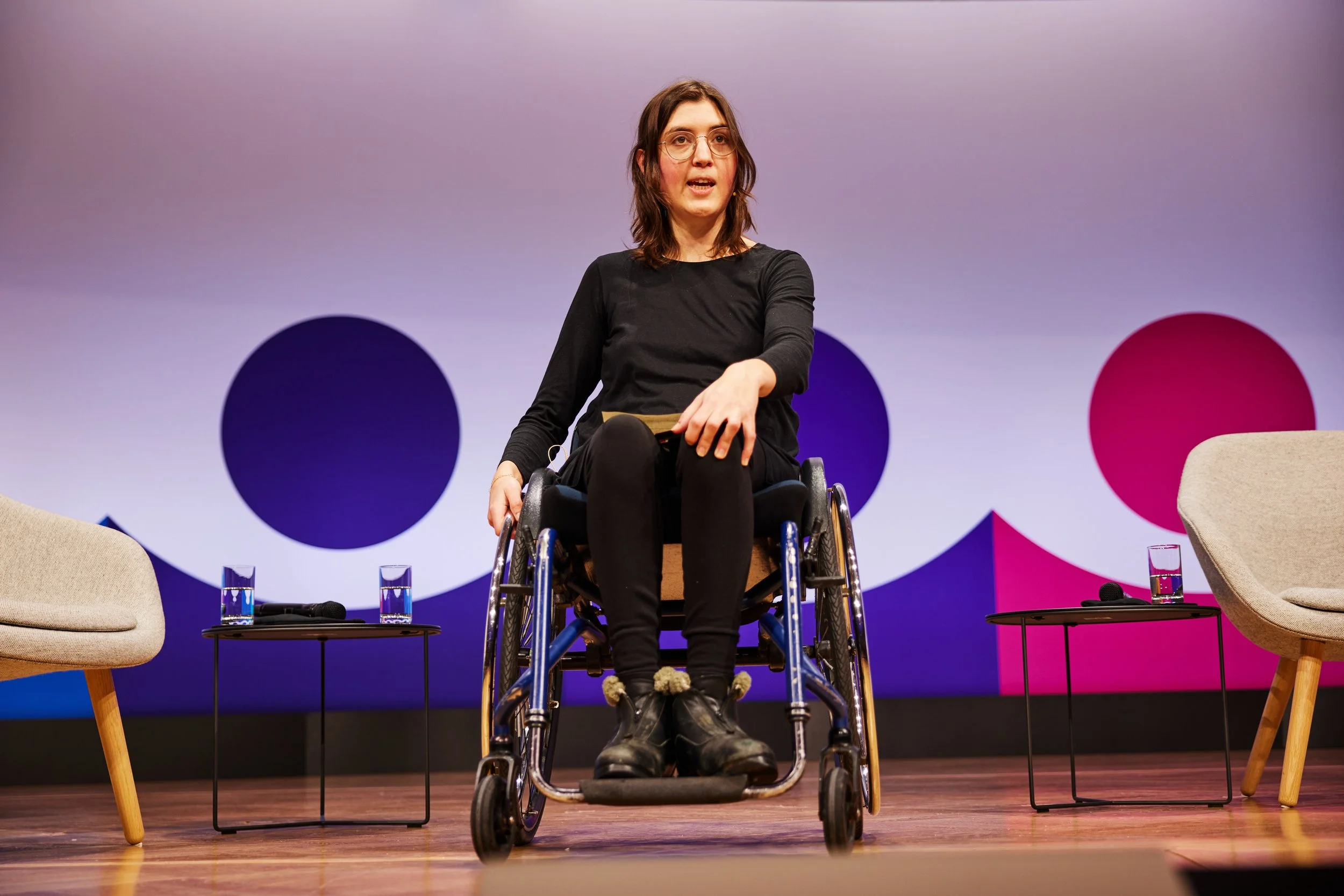Mechthild sitzt im Rollstuhl auf einer Bühne und hält einen Vortrag.