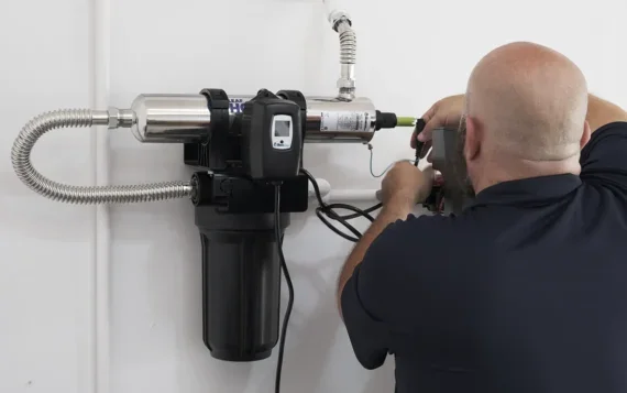 Technician repairing or maintaining a water filtration or purification system mounted on a white wall.
