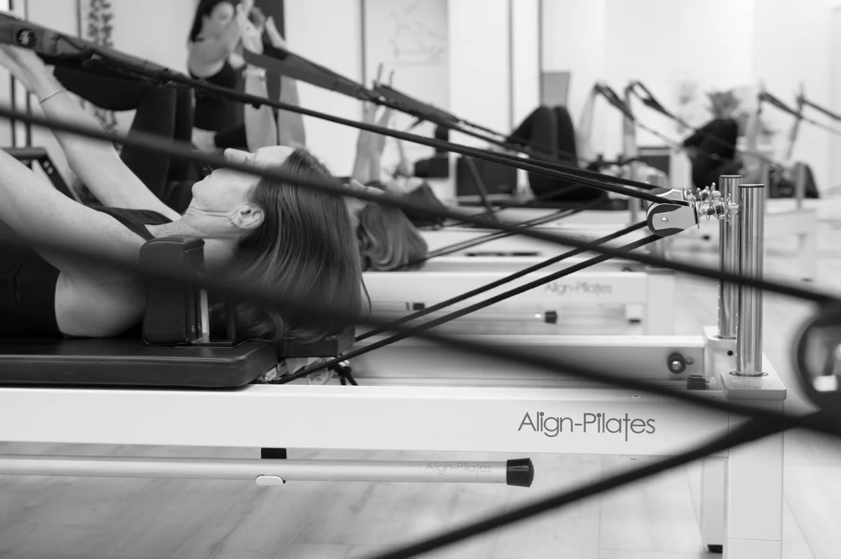 Editorial photograph of a reformer Pilates session showing the instructor and studio environment