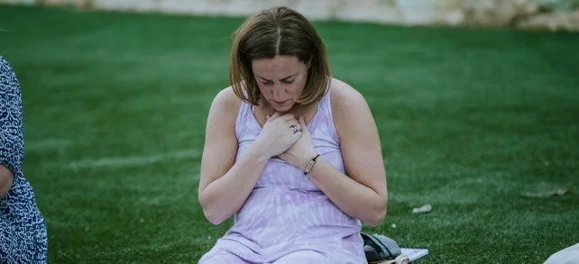 woman kneeling on grass with head bowed and holding her hands over her chest