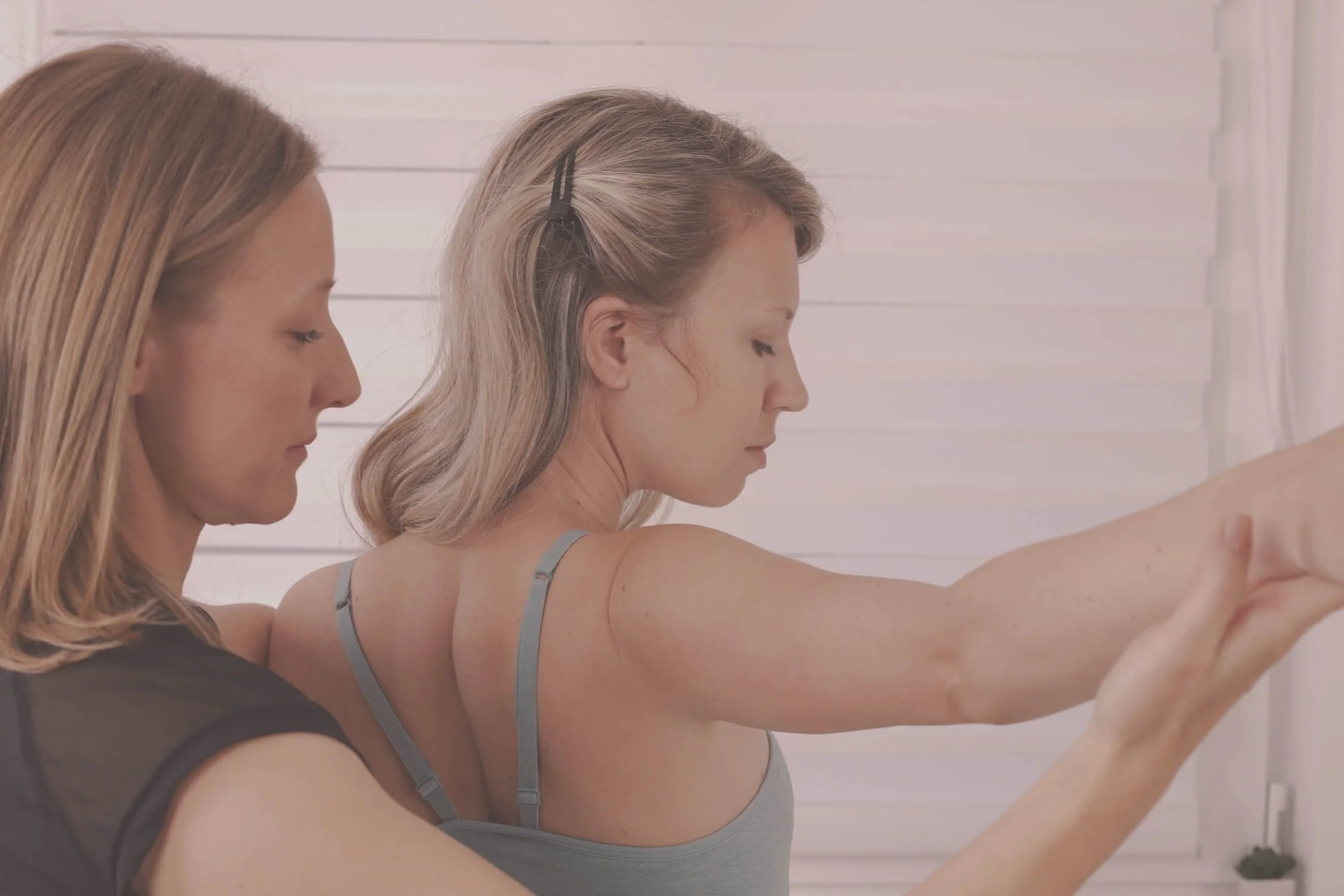 Seitenprofil einer blonden Trainerin, die während einer Physiotherapie- oder Bewegungssitzung sanft den ausgestreckten Arm einer Frau hält und führt.