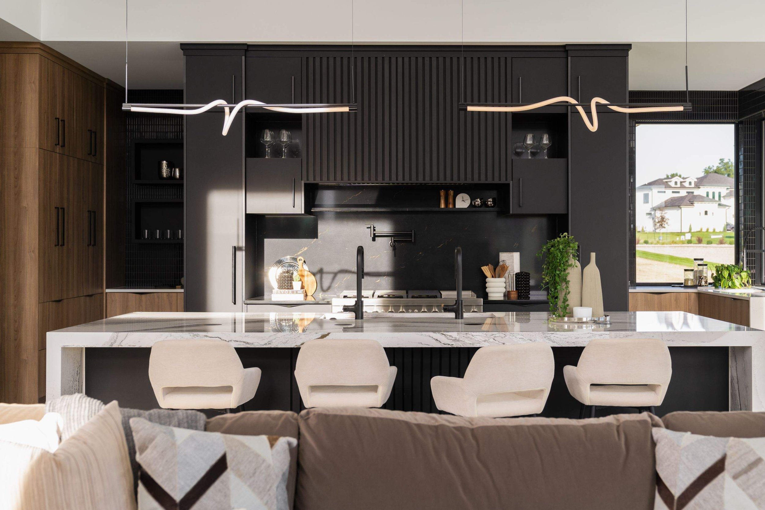 This contemporary kitchen blends bold black cabinetry with sleek pendant lights that provide focused illumination. The design highlights the marble countertops and ensures functionality meets aesthetics.