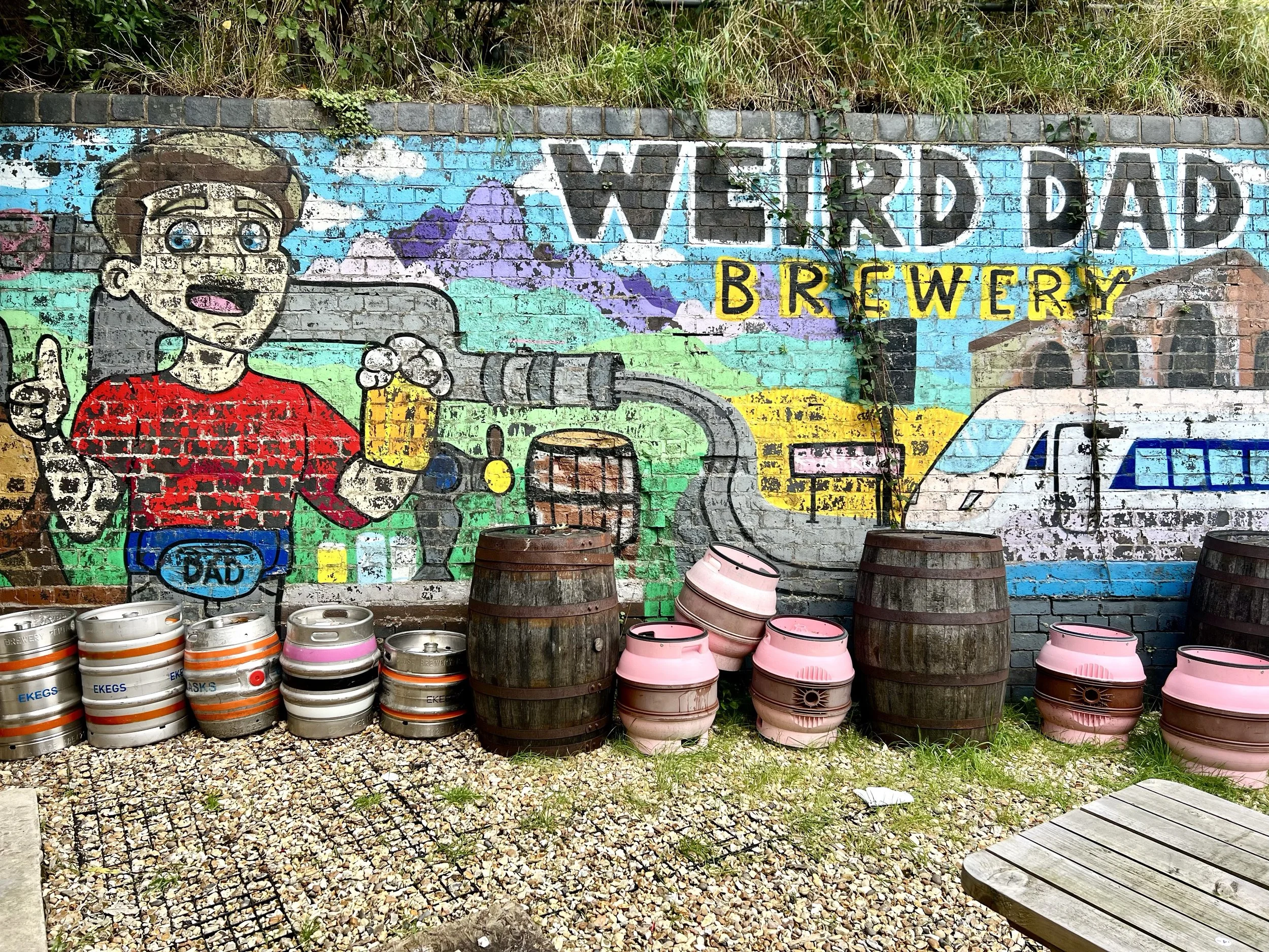 Outdoor seating, empty Casks and Kegs with a Weid Dad mural on the wall behind them.