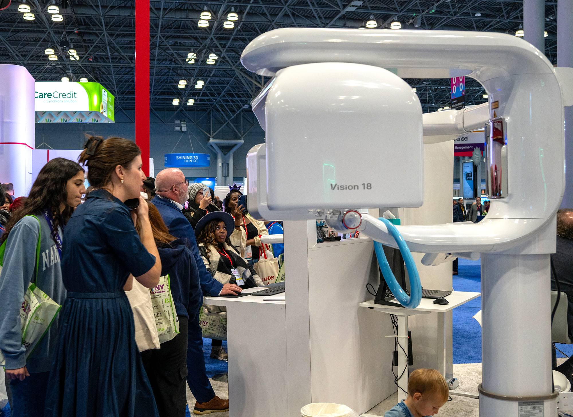 A large medical imaging machine labeled 'Vision 18' at a busy trade show or conference, with a crowd of people watching.