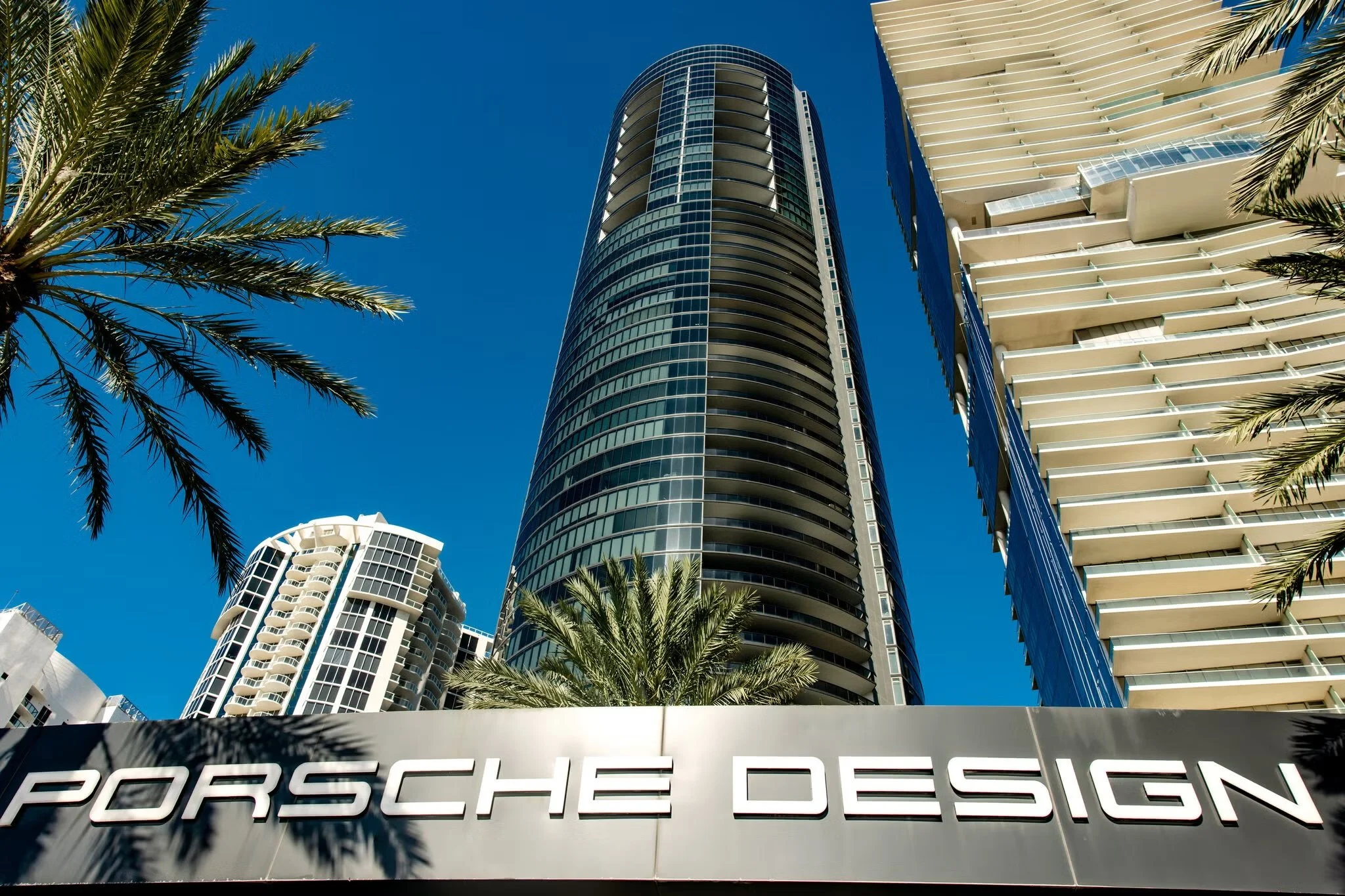 A glass condo tower in Miami with a sign in front saying "Porsche Design"