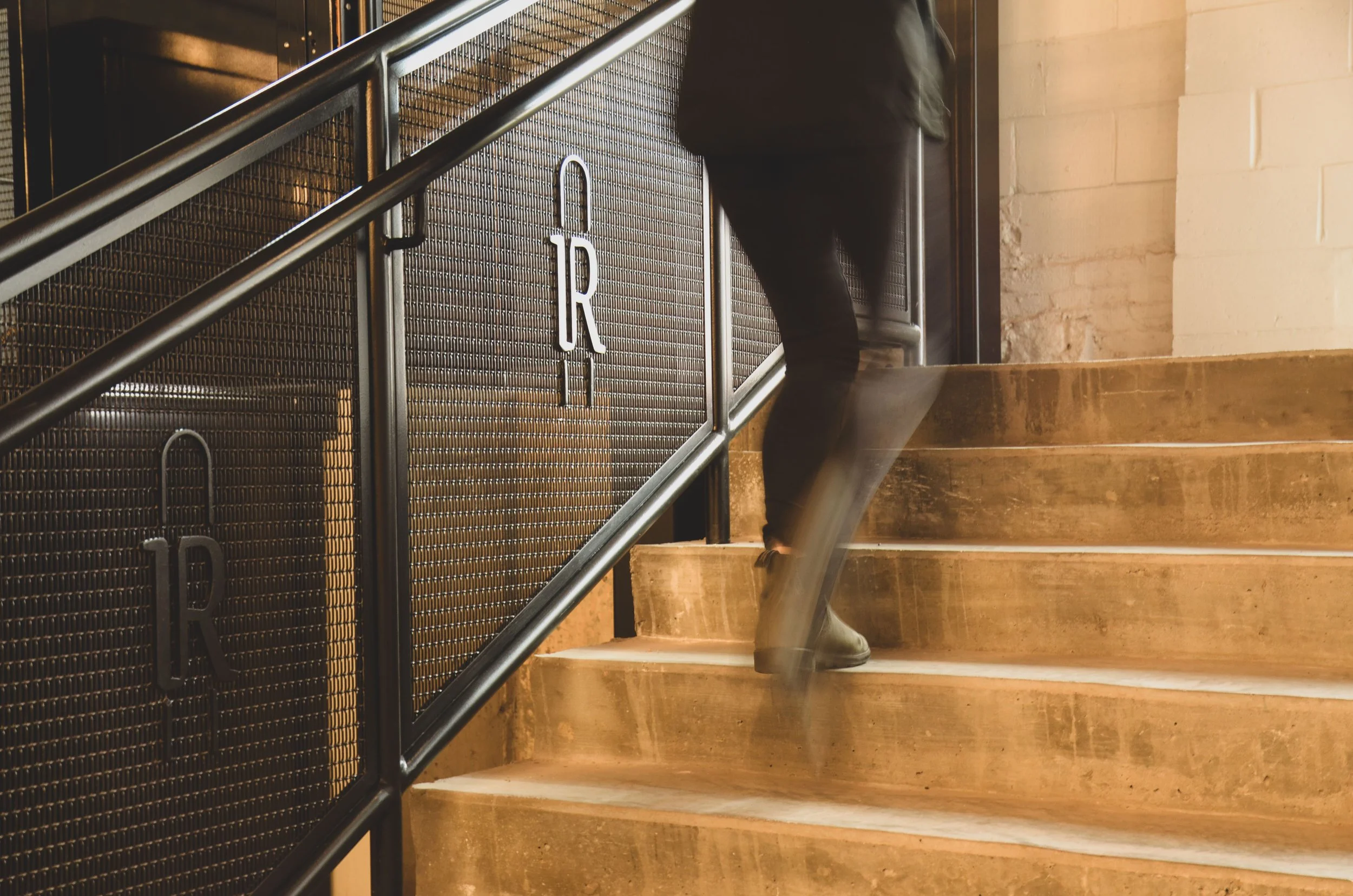 Woman walking up concrete stairs with a metal railing with a building logo.