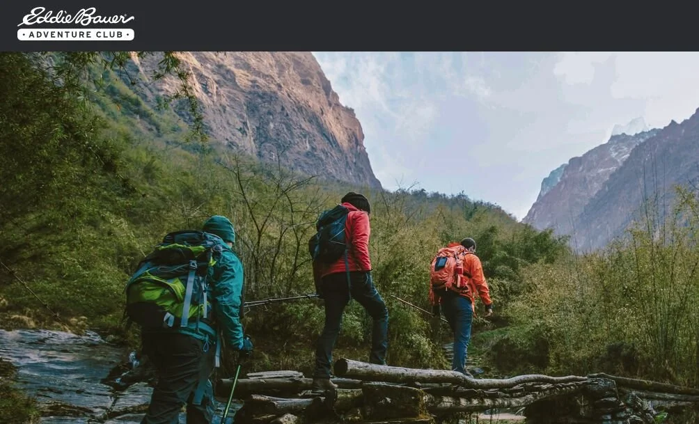 Three hikers near a mountain with an Eddie Bauer Adventure Club logo at the top left of the image