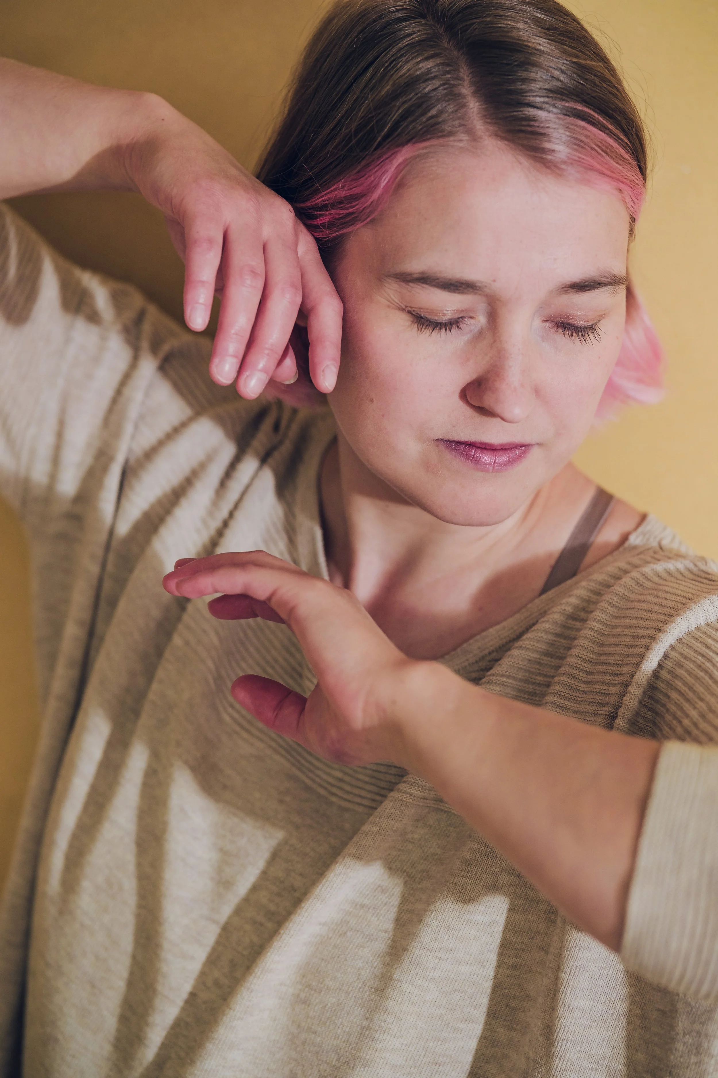 Mimmi Salo lähikuvassa silmät kiinni, kädet kasvojen lähellä, päällä beige paita ja hiuksissa vaaleanpunaiset raidat