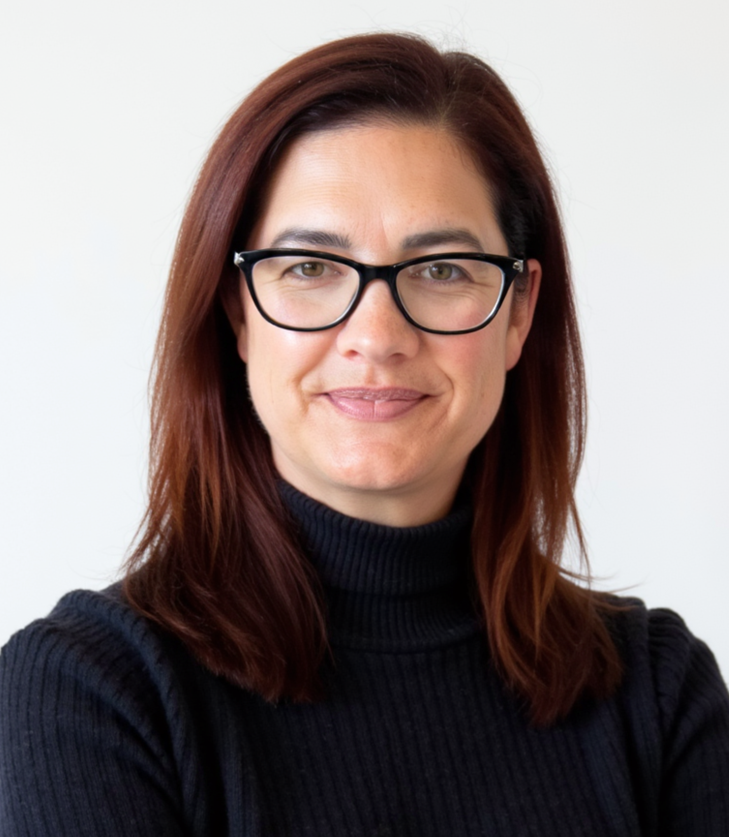 Photograph of a woman with shoulder-length auburn hair, wearing black glasses and a black turtleneck sweater, smiling against a plain white background.