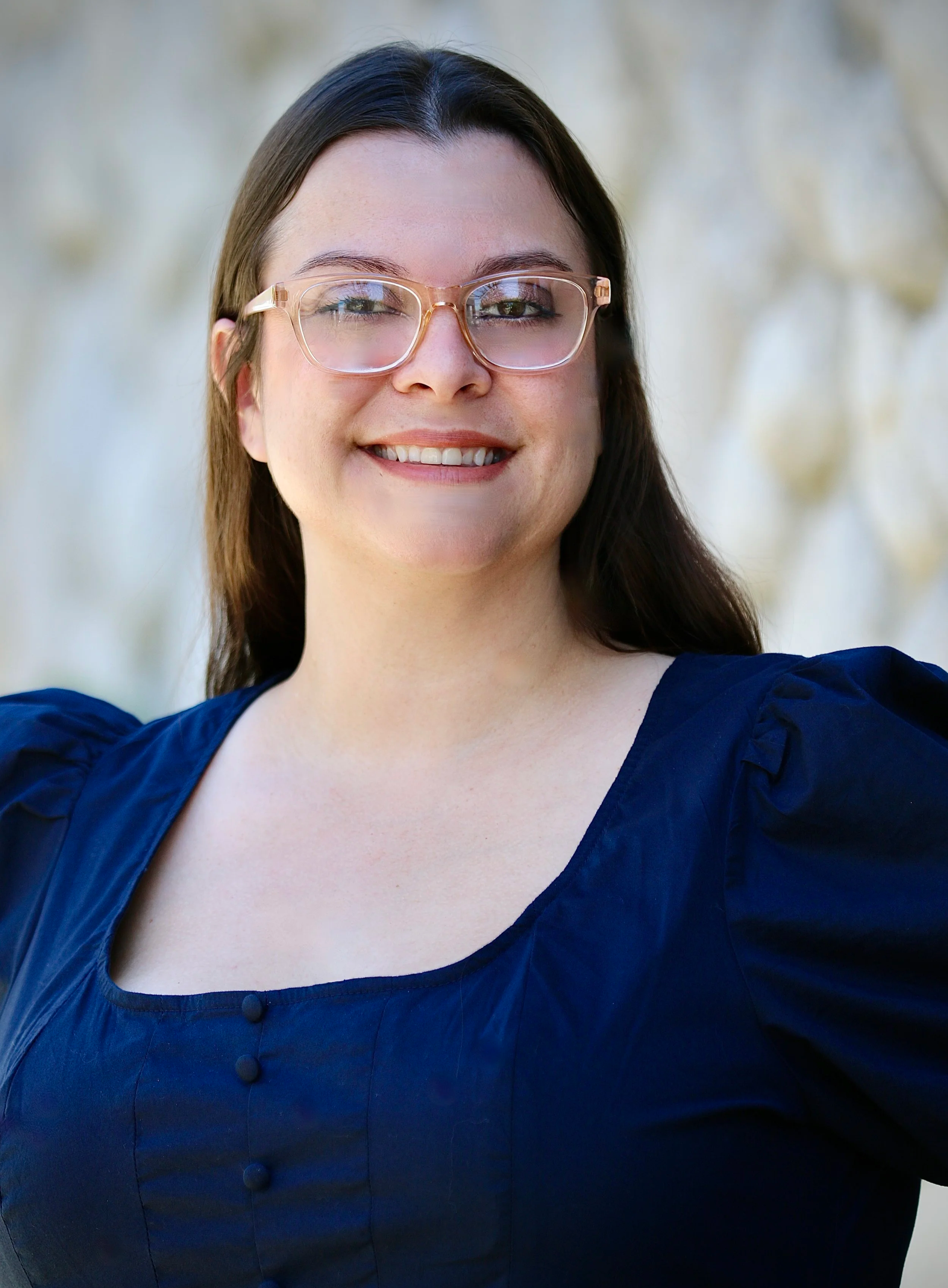A woman with long brown hair, glasses, and earrings standing outdoors in front of a tree with green leaves. She is wearing a black shirt with a name tag that reads 'Crystal Hardy, Foothill Family Shelter, Case Manager.' She is smiling at the camera.