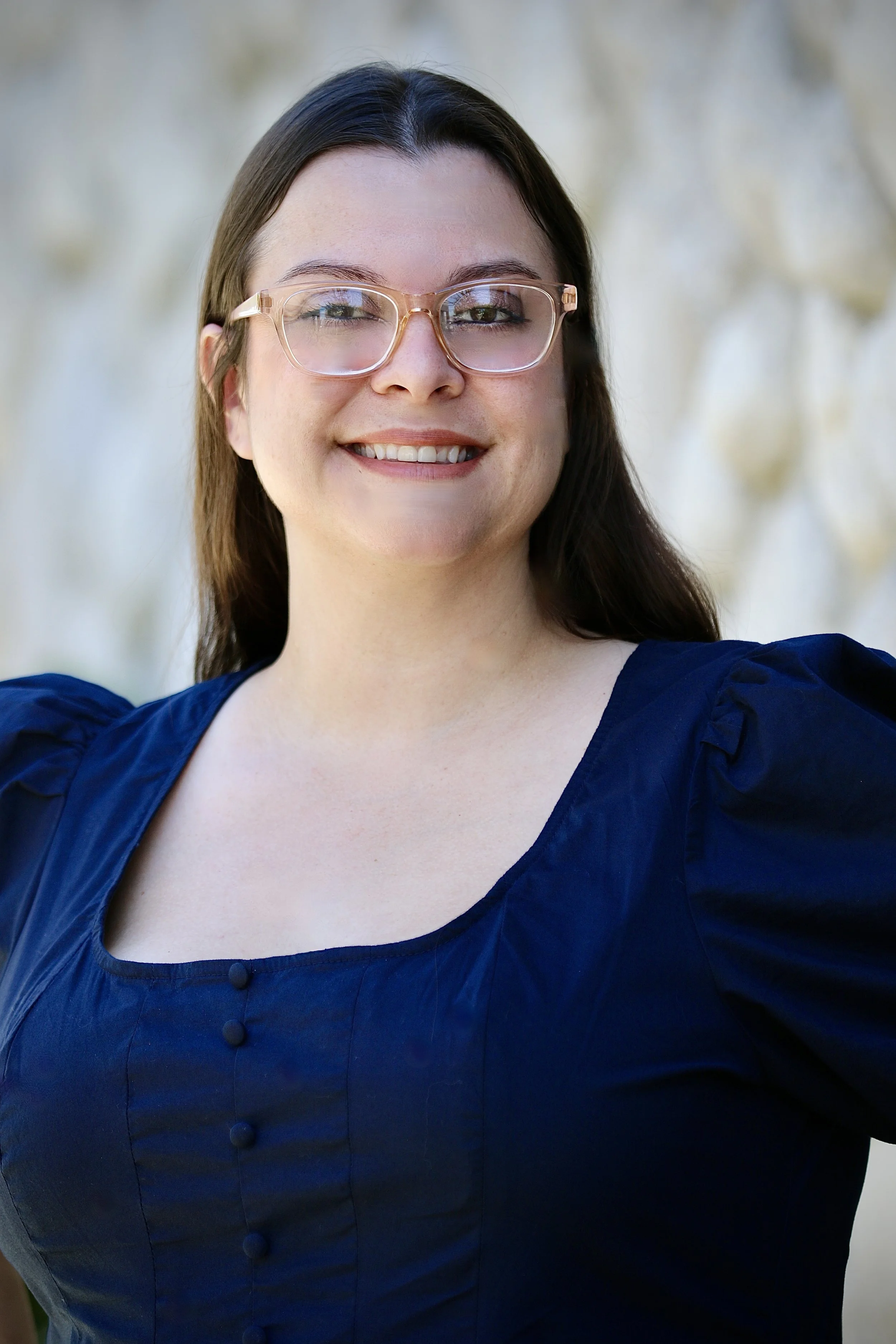 A woman with long brown hair, glasses, and earrings standing outdoors in front of a tree with green leaves. She is wearing a black shirt with a name tag that reads 'Crystal Hardy, Foothill Family Shelter, Case Manager.' She is smiling at the camera.