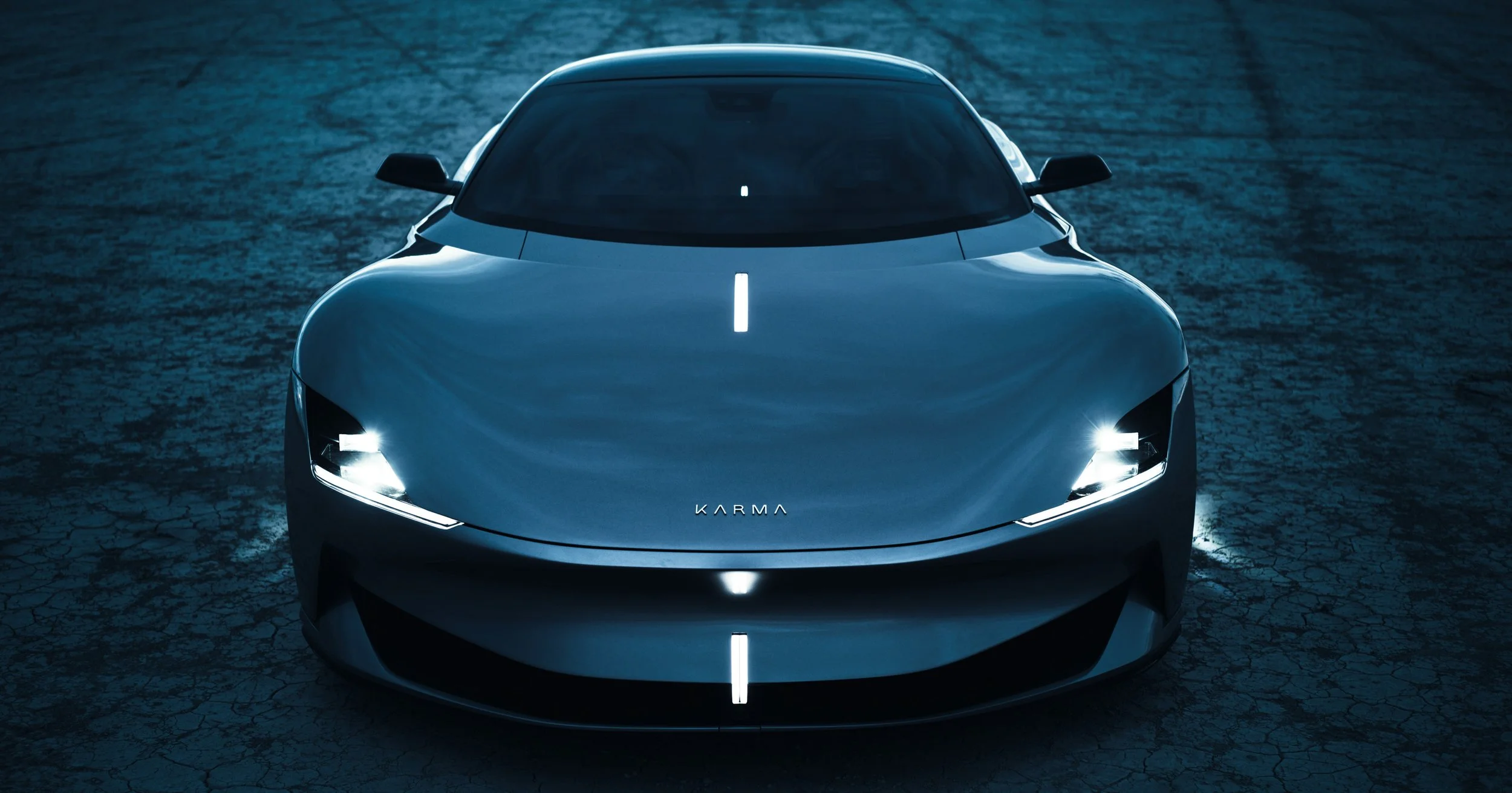 A sleek, futuristic electric car with the word 'KARMA' on the front, parked on a cracked, dark surface under moody lighting.