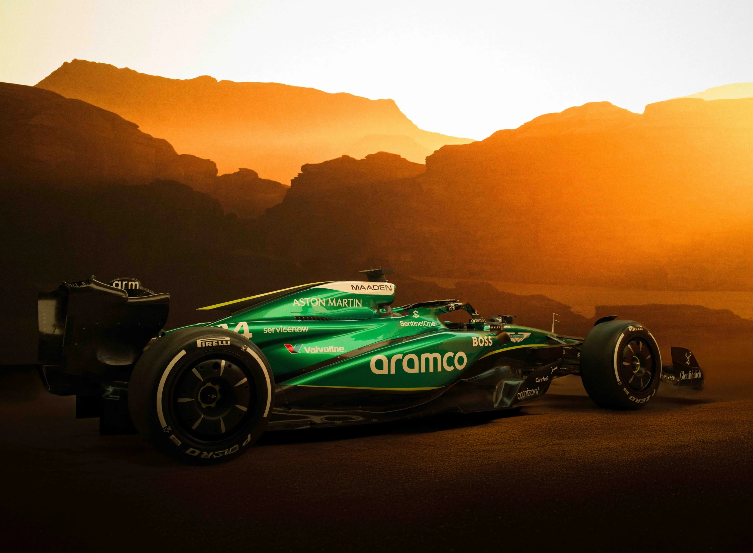 A green Formula 1 race car with sponsor logos, set against a desert canyon landscape background.