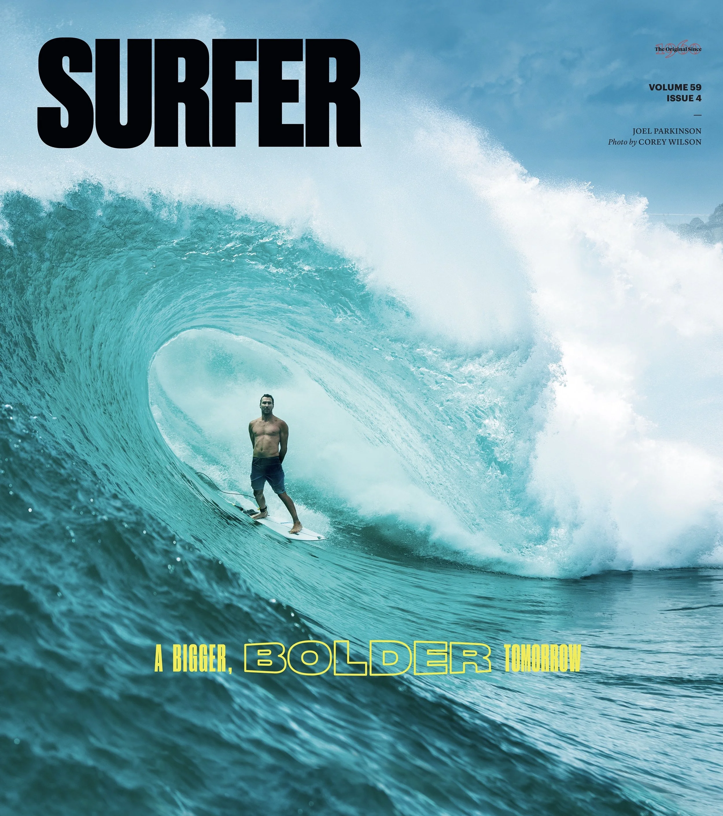 A surfer riding inside a large ocean wave with a clear sky in the background, text overlay reading 'SURFER' and 'A BIGGER BOLDER TOMORROW'.