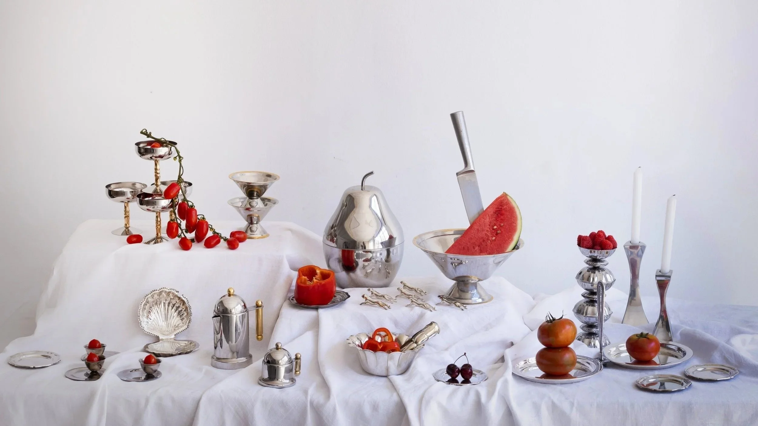 Mesa decorada con objetos de plata, frutas y velas, en un estilo elegante y minimalista.