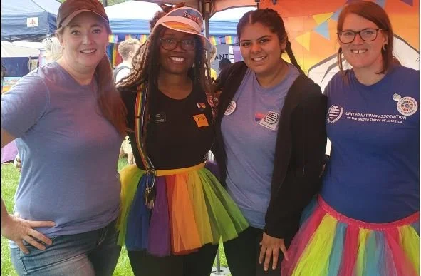 Four smiling people stand wearing rainbow tutu's at a UNA Boulder event.JPG
