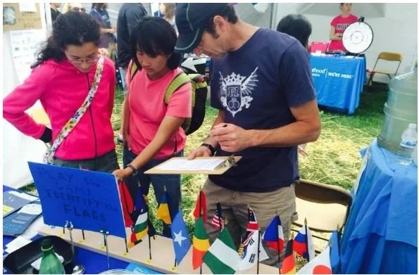 Three people stand viewing a UNA table at a community event.
