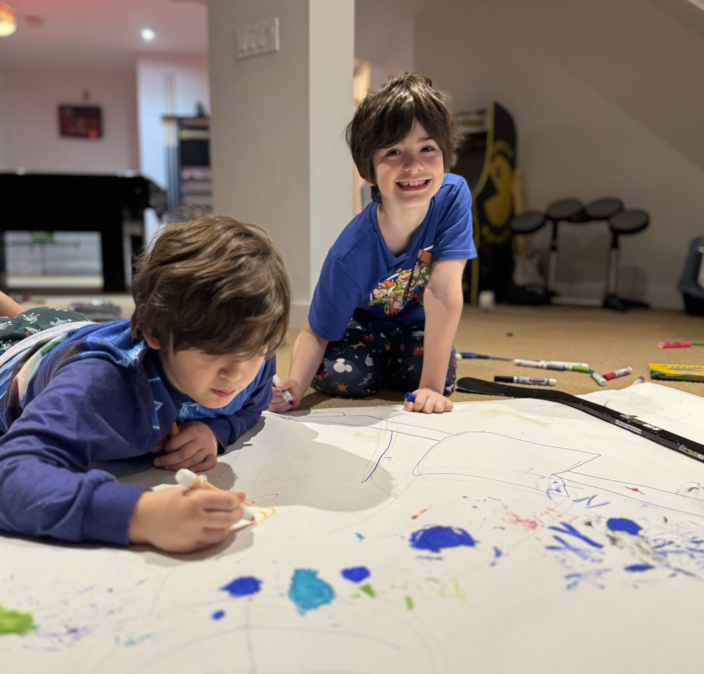 Children drawing and painting together on large paper at table, representing creativity development, learning through visuals and playful visual expression aligned with Visual Versa principles