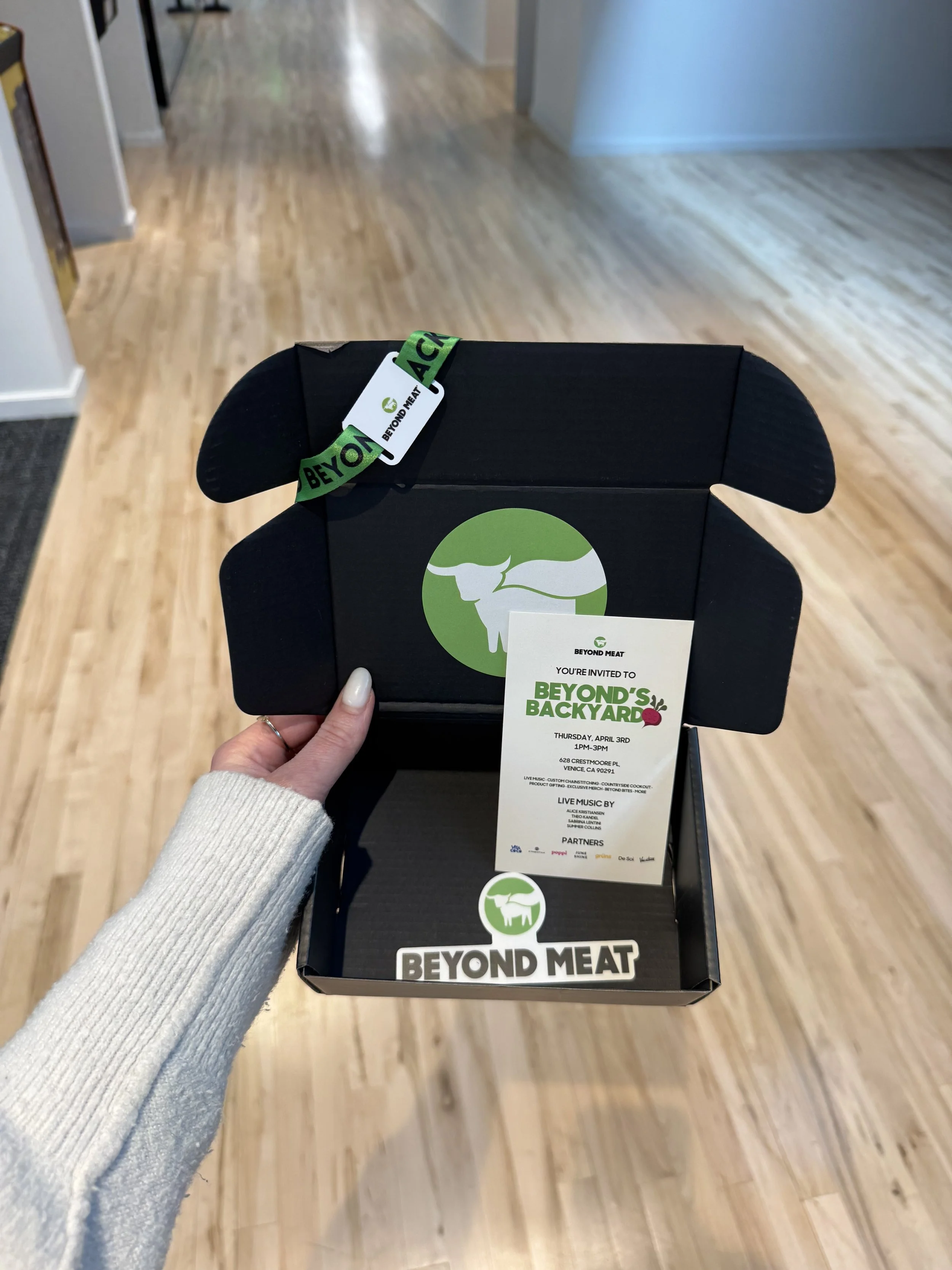 Open black box with green and white Beyond Meat logo, inside is an invitation card for an event called 'Beyond's Backyard' with details and supporting logos.
