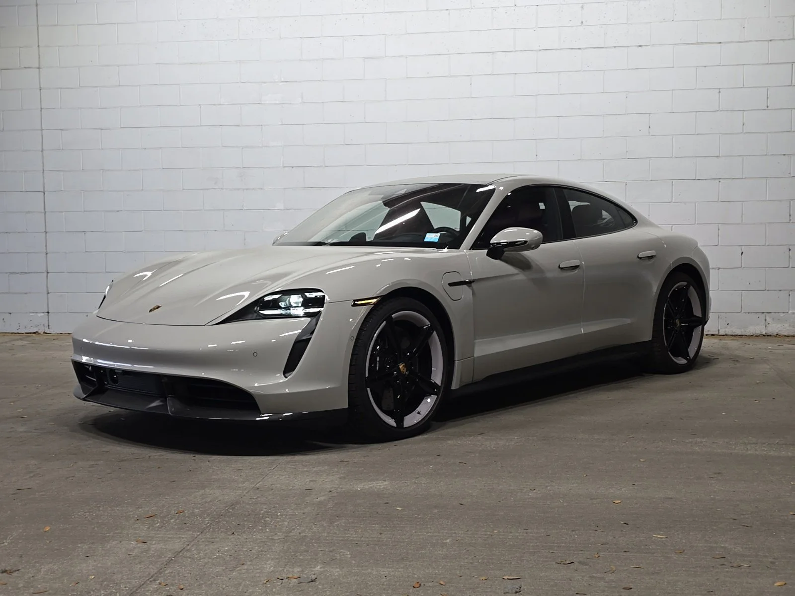 White Porsche electric sports car parked indoors against a white cinder block wall.