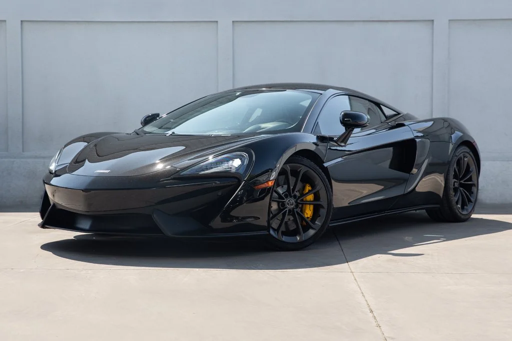 Black sports car parked on pavement in front of a gray wall.