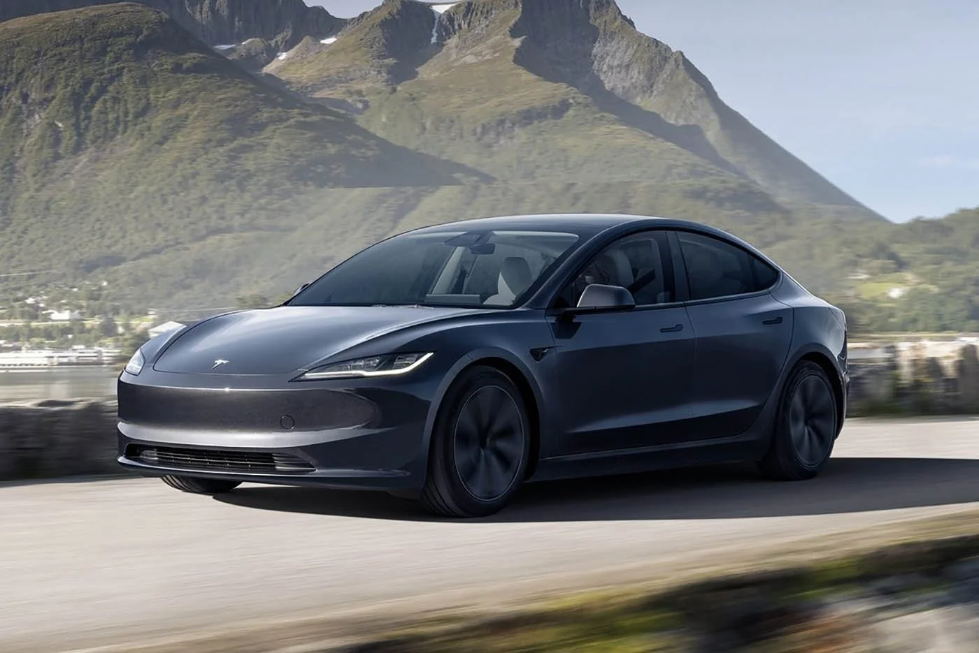 A sleek black Tesla Model 3 driving on a road with mountains in the background.